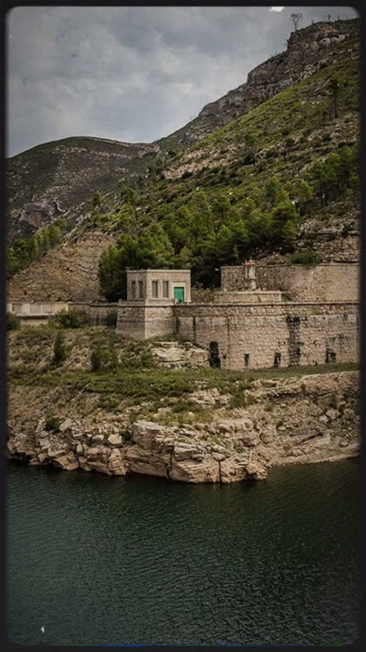 Embalse al pie de la montaña, con una construcción de piedra junto al agua.