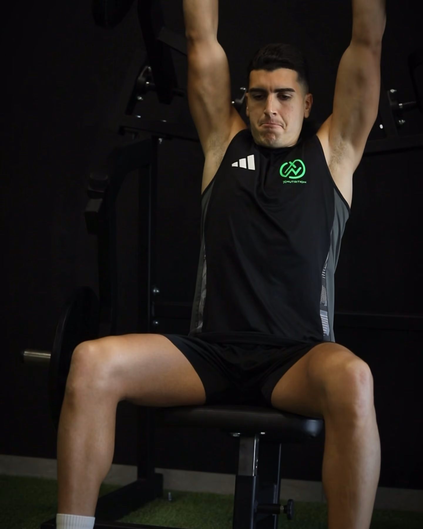 Press de hombros sentado con barra, en la penumbra de un gimnasio.